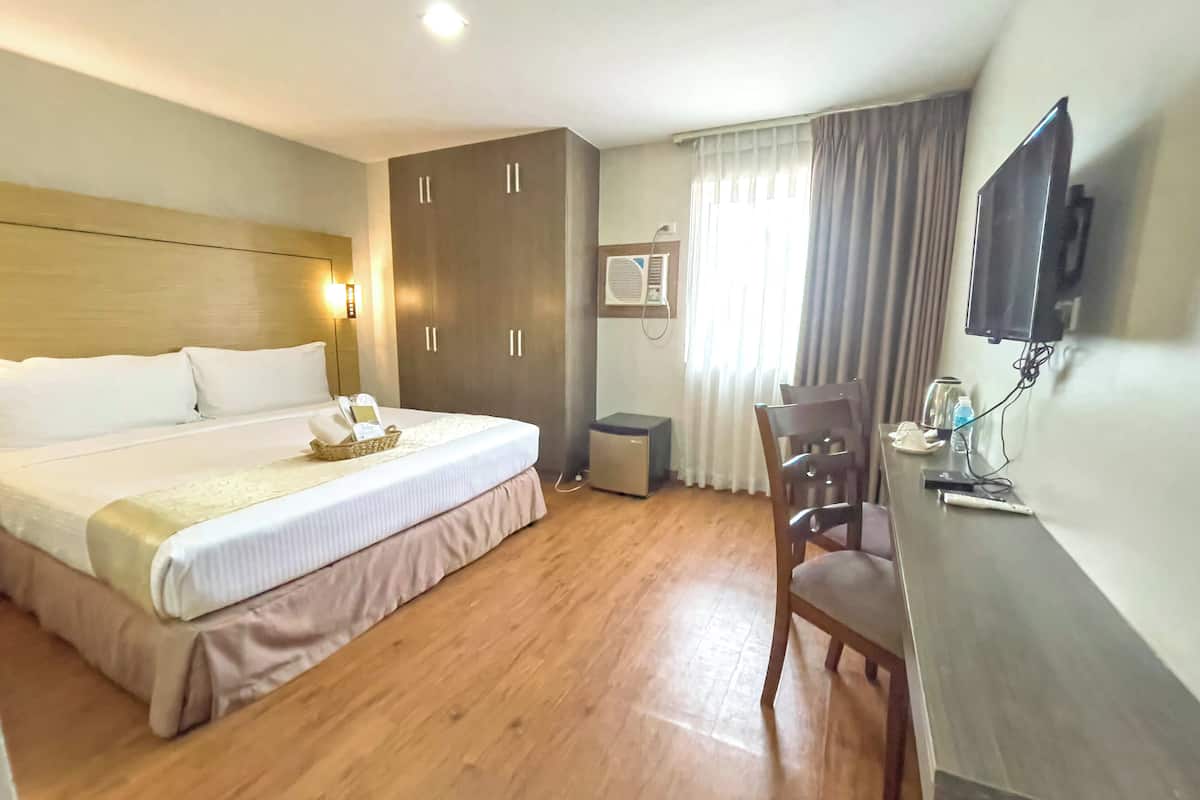 A hotel room with a large bed, a desk with a chair, a television, and an air conditioning unit.