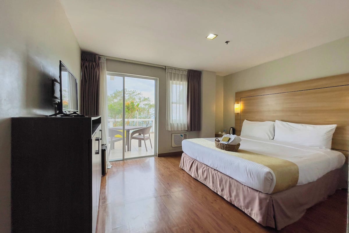 A hotel room with a large bed, a desk, and a balcony with a table and chairs.