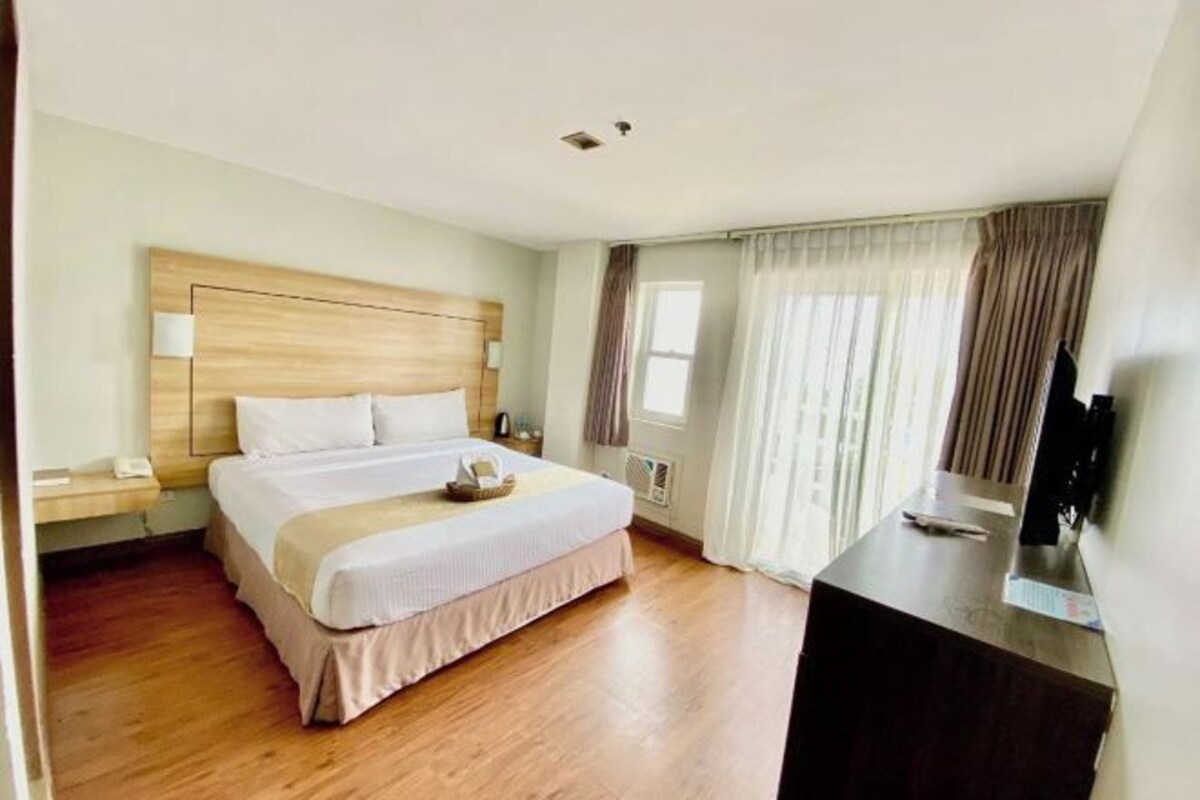 A hotel room with a wooden bed, a desk, and a television.