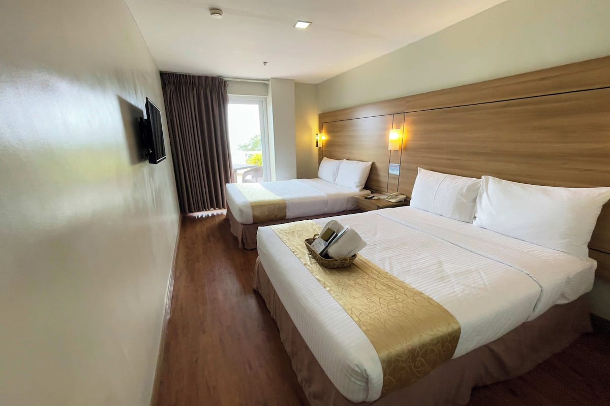 A hotel room with two beds, a TV mounted on the wall, and a window with curtains.
