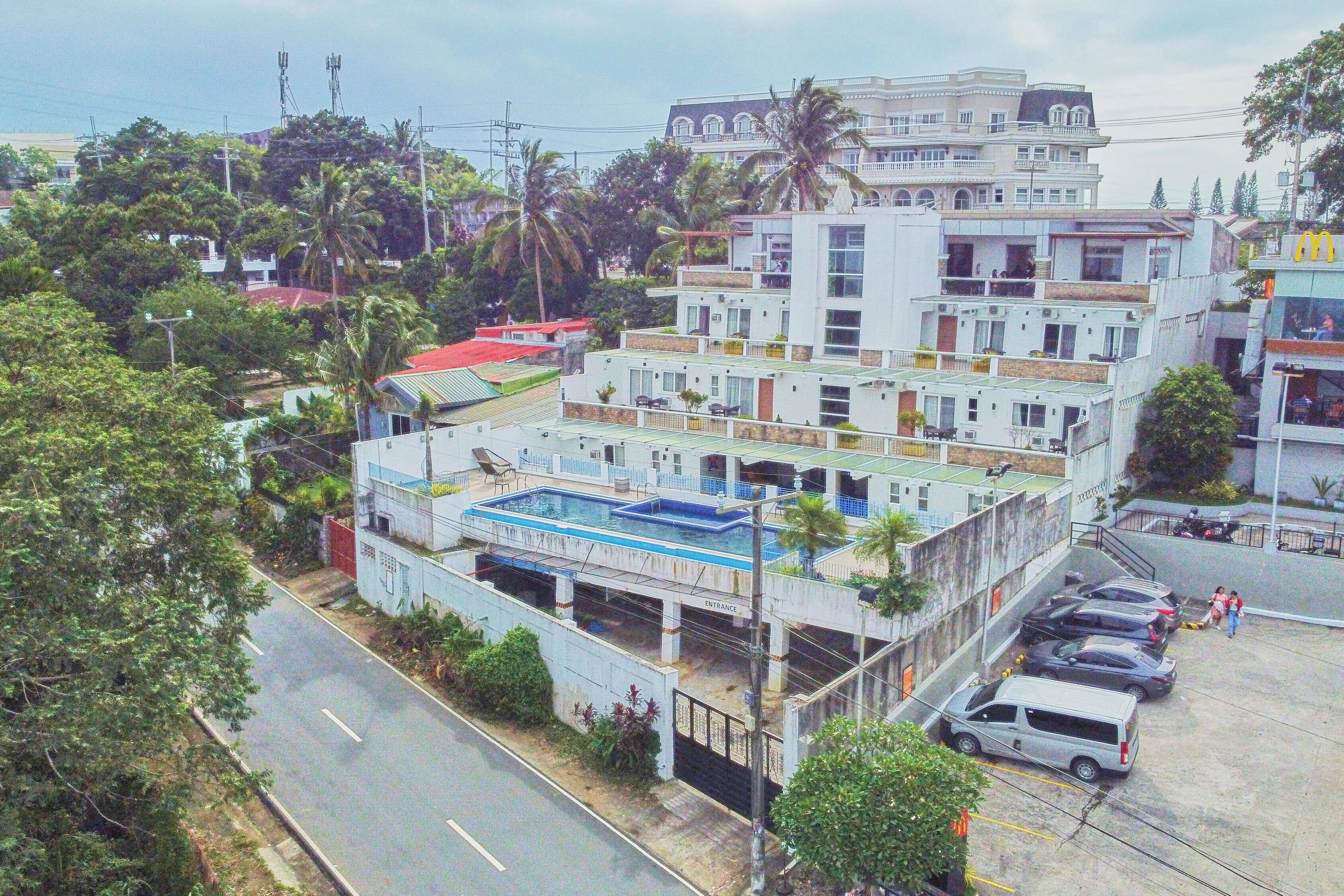 A multi-story building with a swimming pool, parking area, and a street view.