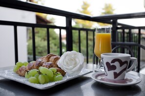Un plateau de petit-déjeuner avec des croissants, des raisins et une rose blanche, posé sur une table de balcon.