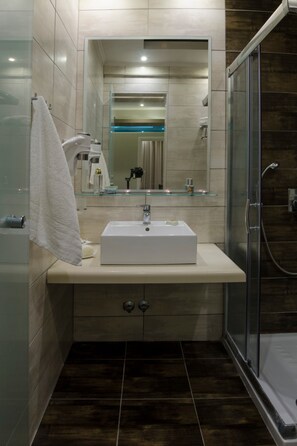 Une salle de bain moderne avec une douche à l’italienne en verre, un lavabo blanc avec un miroir au-dessus, et une serviette accrochée au mur.