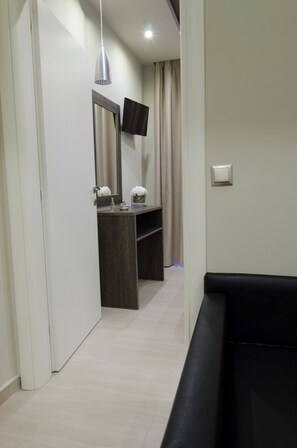 Un pasillo con un tocador de madera oscura, un espejo, un televisor de pantalla plana y una cortina color beige.