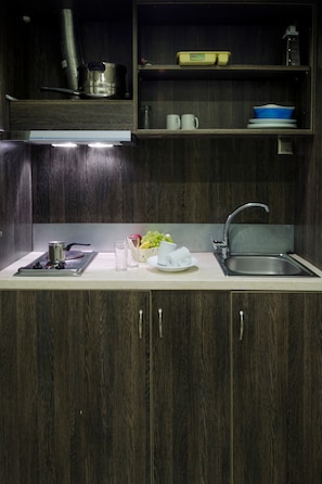A kitchen with a stainless steel sink, a stove, and a countertop with a glass, a bowl of fruit, and some utensils.