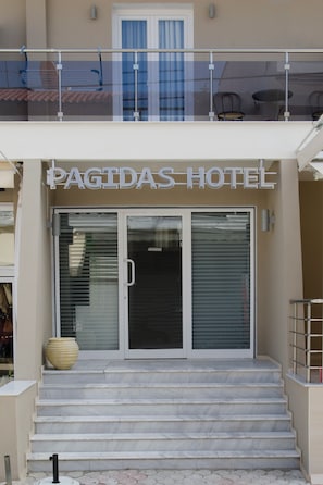A hotel entrance with a sign reading 'PAGIDAS HOTEL,' a set of marble steps, and a glass door.