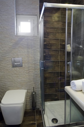 A bathroom with a glass shower enclosure, a toilet, and a towel on the counter.