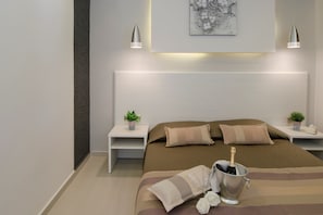A modern bedroom with a large bed, two bedside tables with potted plants, a headboard with integrated lighting, and a framed artwork above the bed. - Apartment '207' with Wi-Fi and Air Conditioning (Halkidiki)