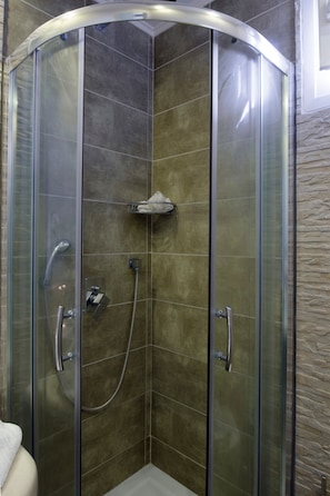 A glass-enclosed shower stall with a handheld showerhead and a wall-mounted faucet.