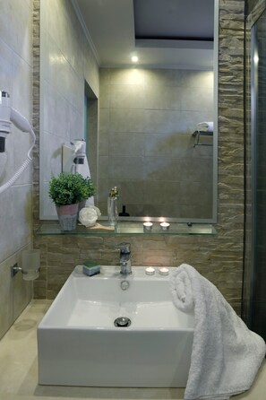 Une salle de bain avec un grand lavabo, un miroir, un sèche-cheveux, une plante en pot et des bougies.