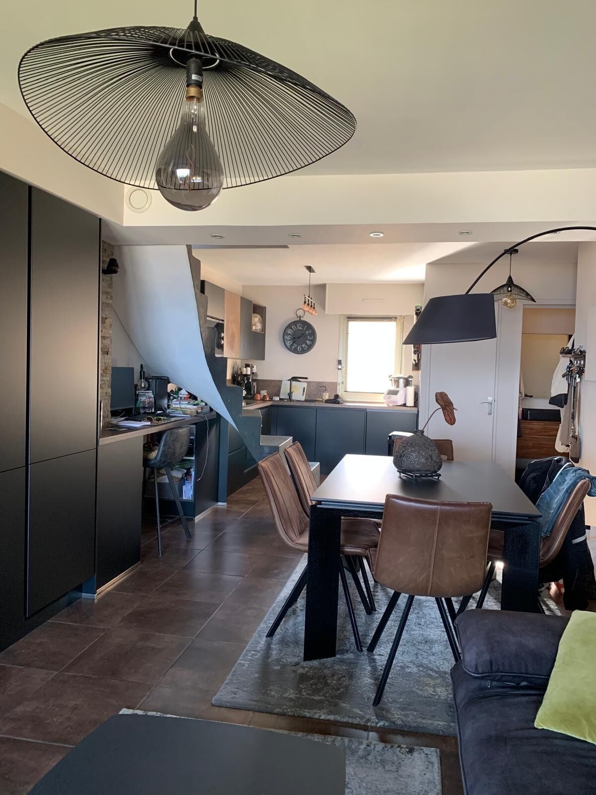 Une cuisine moderne avec un coin repas, comprenant un grand îlot central, des meubles de rangement aux couleurs sombres et un luminaire suspendu.