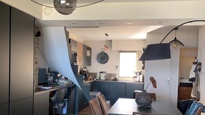 A modern kitchen with a dining area, featuring a large island, dark cabinetry, and a hanging light fixture.