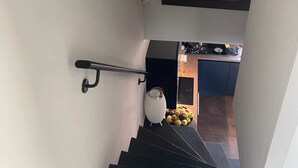 A staircase with a handrail, a framed artwork above, and a kitchen area with a fruit bowl visible.