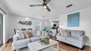 Ein modernes Wohnzimmer mit einem grauen Ecksofa, einem weißen Couchtisch und einem Deckenventilator.