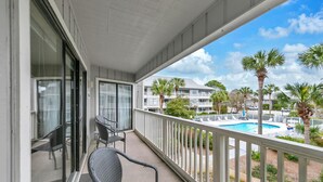 Ein Balkon mit Blick auf einen Swimmingpool, Palmen und ein mehrstöckiges Gebäude.