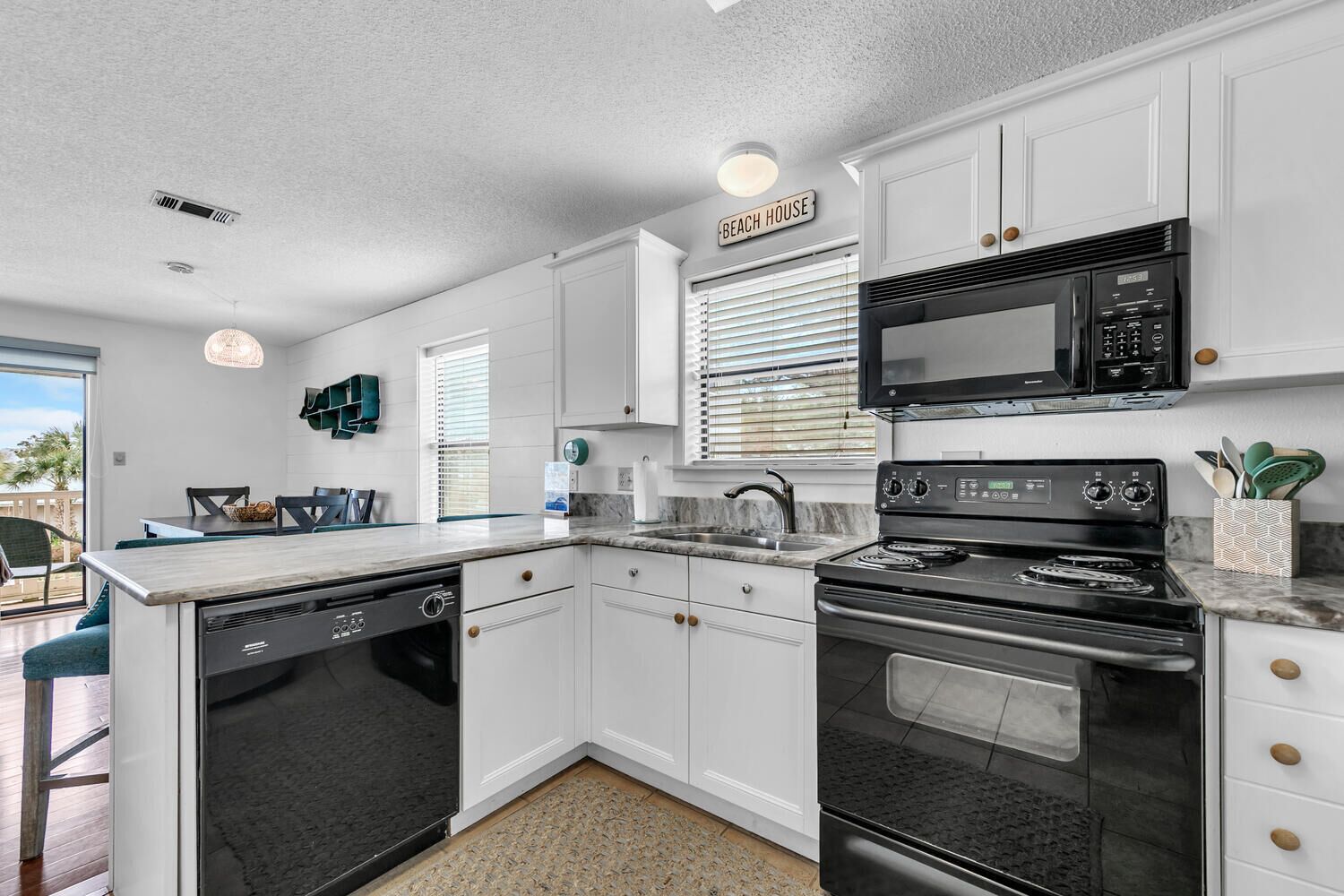 A compact kitchen with white cabinets, a black microwave, a stove, and a dishwasher.