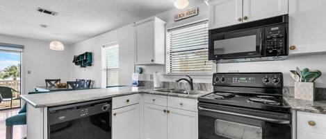 A compact kitchen with white cabinets, a black microwave, a stove, and a dishwasher.