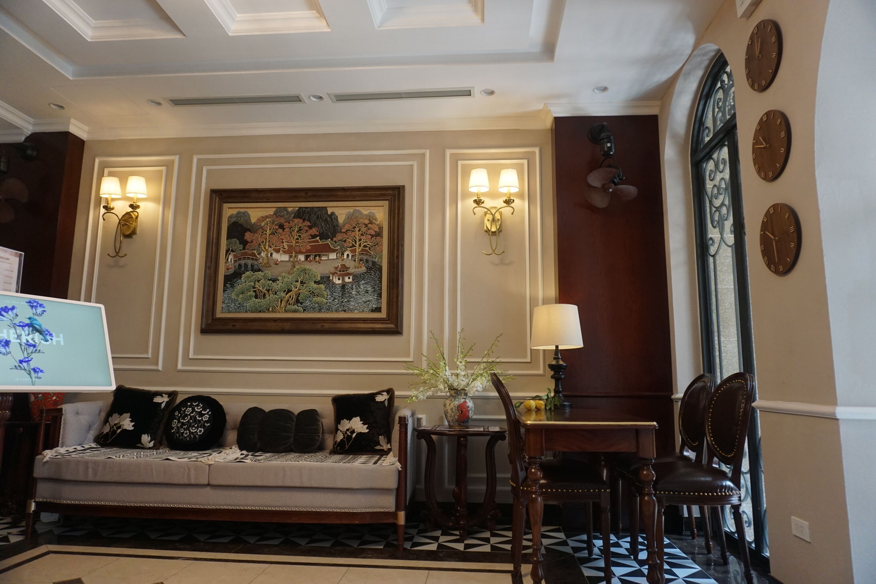 A hotel lobby with a sofa, a dining table, wall-mounted clocks, and a painting.
