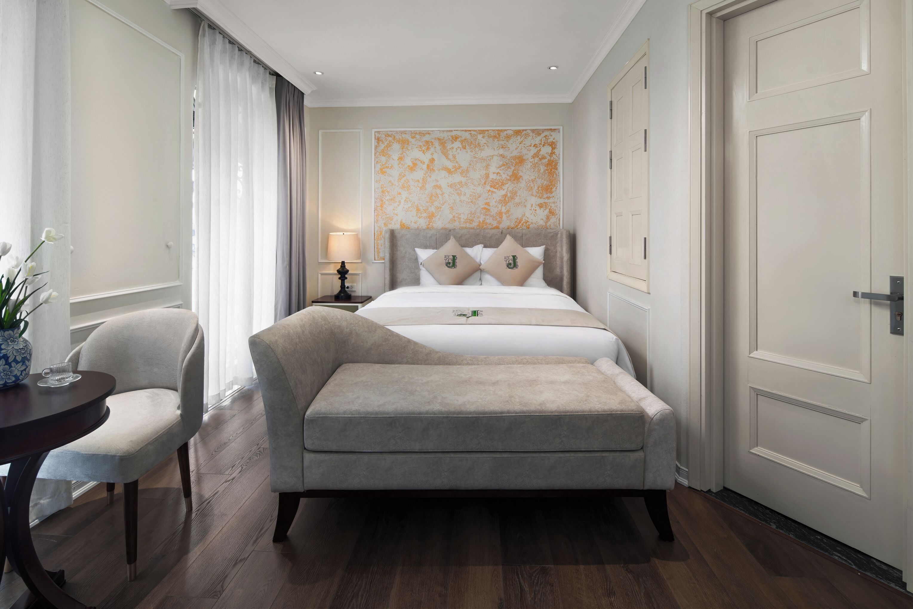 A hotel room with a bed, a chair, a table, and a lamp.
