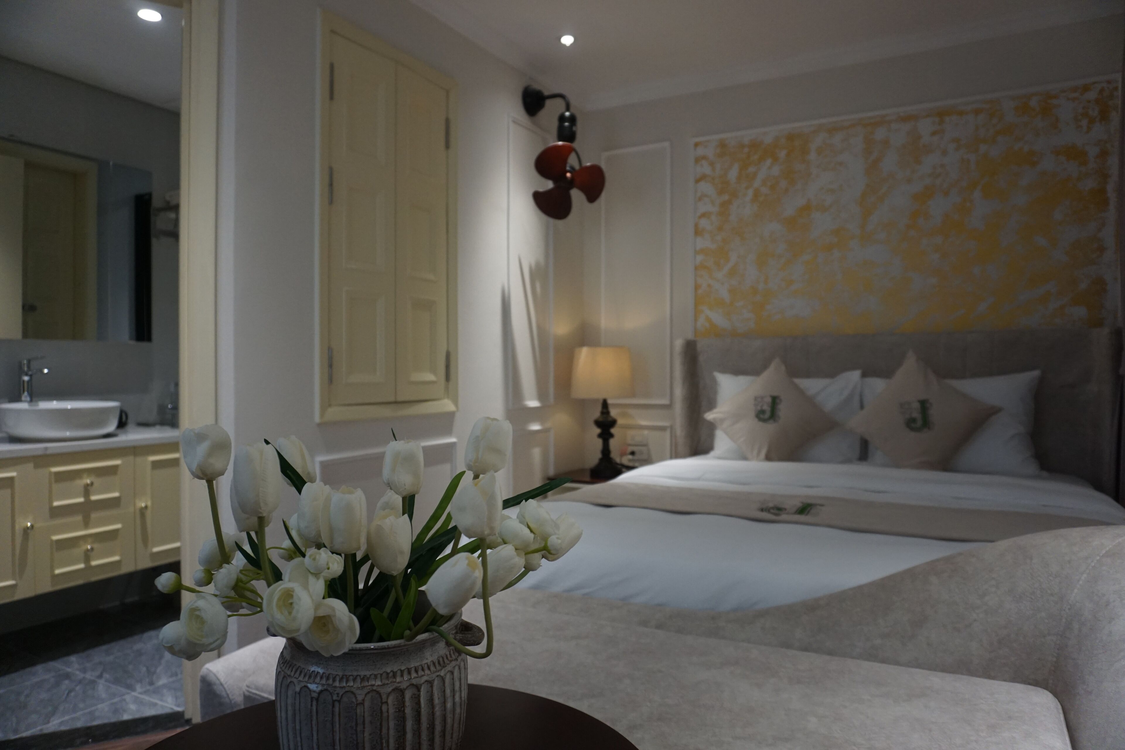 A bedroom with a bed, bedside table, lamp, and a vase with flowers.