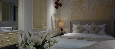 A bedroom with a bed, bedside table, lamp, and a vase with flowers.