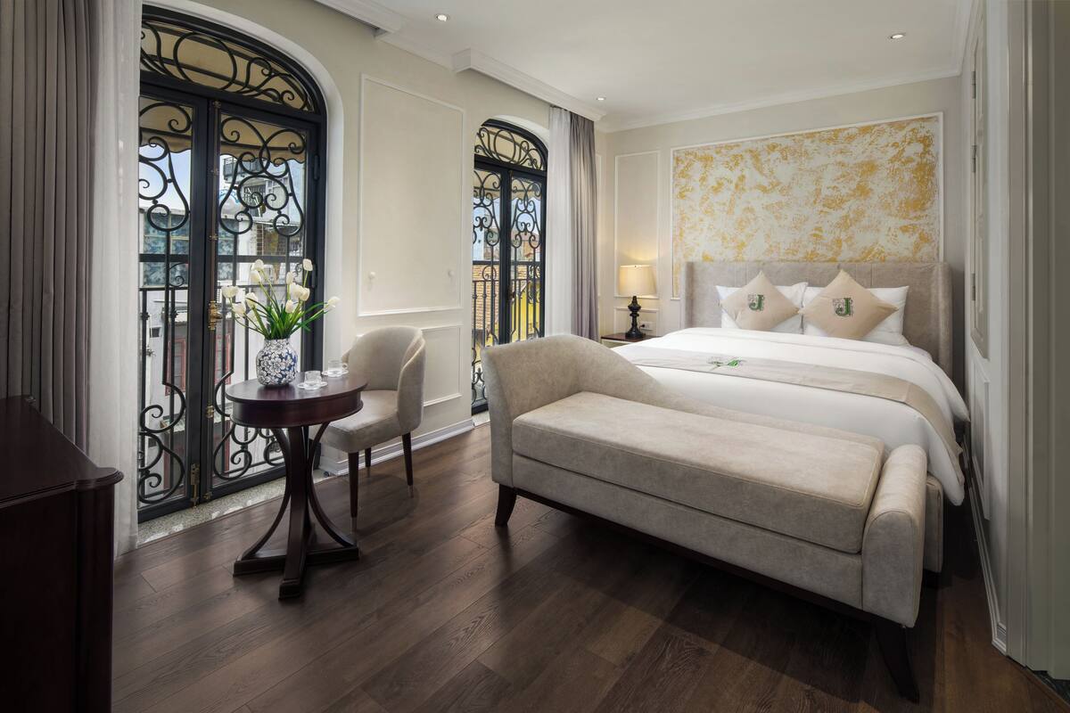 Una habitación de hotel con cama, sofá, una mesita con un florero y una silla.