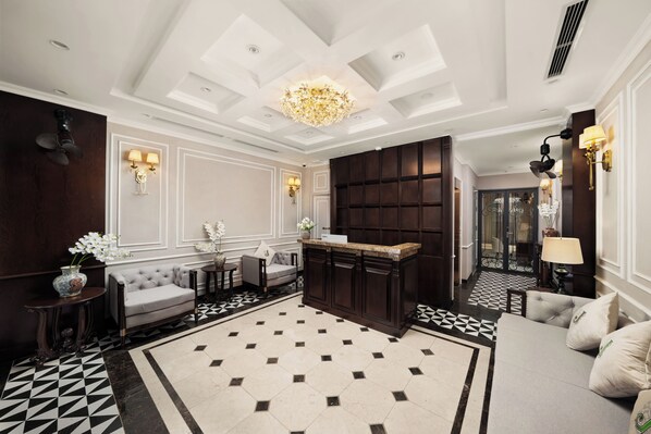 A lobby with a geometric patterned floor, a tufted sofa, a dark wood reception desk, and a chandelier. - Jade Boutique Hotel (Hanoi)