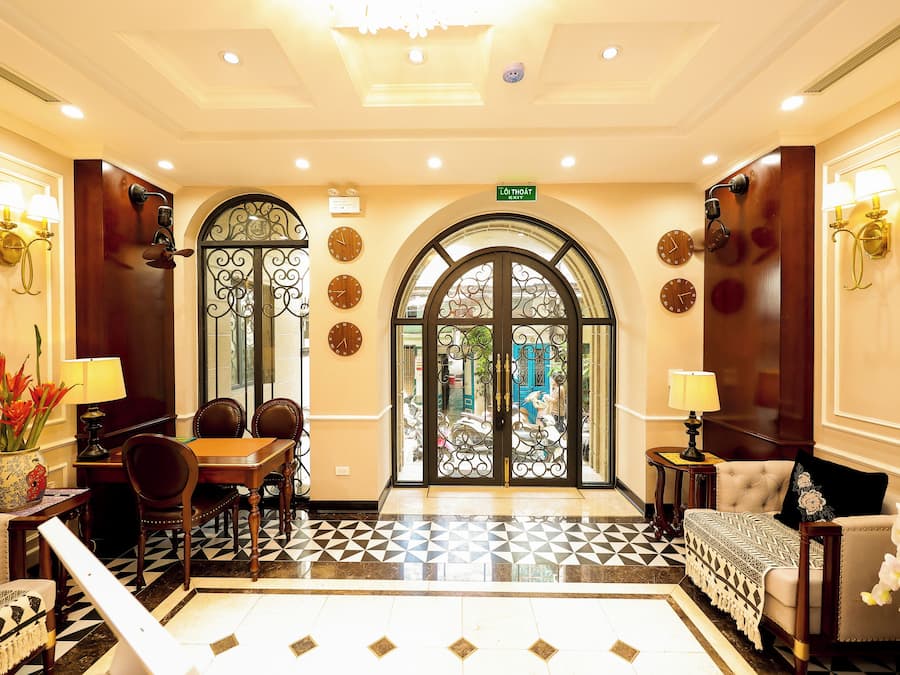 A hotel lobby with a checkered floor, a dining area with a table and chairs, and a reception desk.