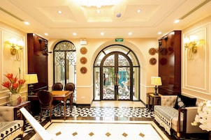 A hotel lobby with a checkered floor, a dining area with a table and chairs, and a reception desk.