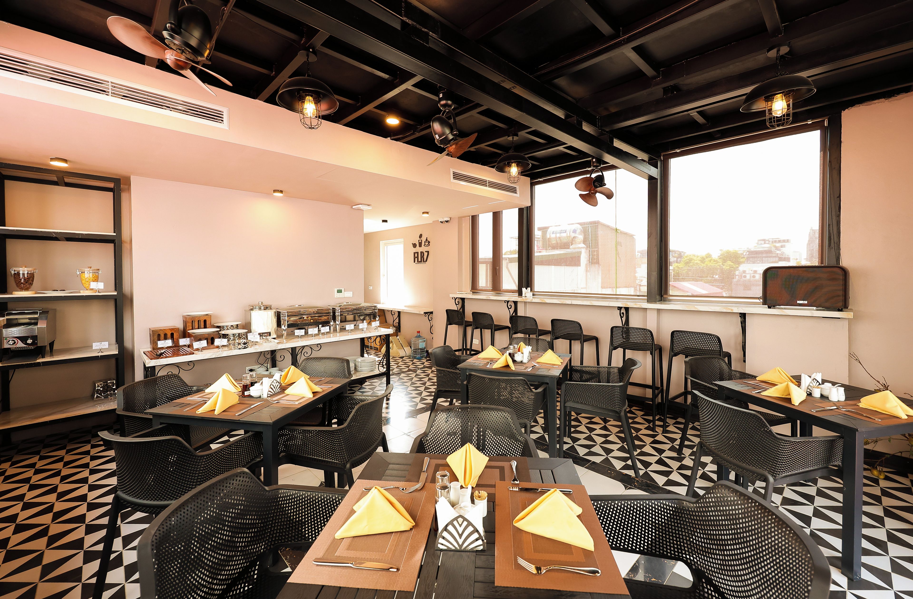 Een restaurant met zwart-wit betegelde vloer, zwarte stoelen en tafels voorzien van gele servetten en bestek.