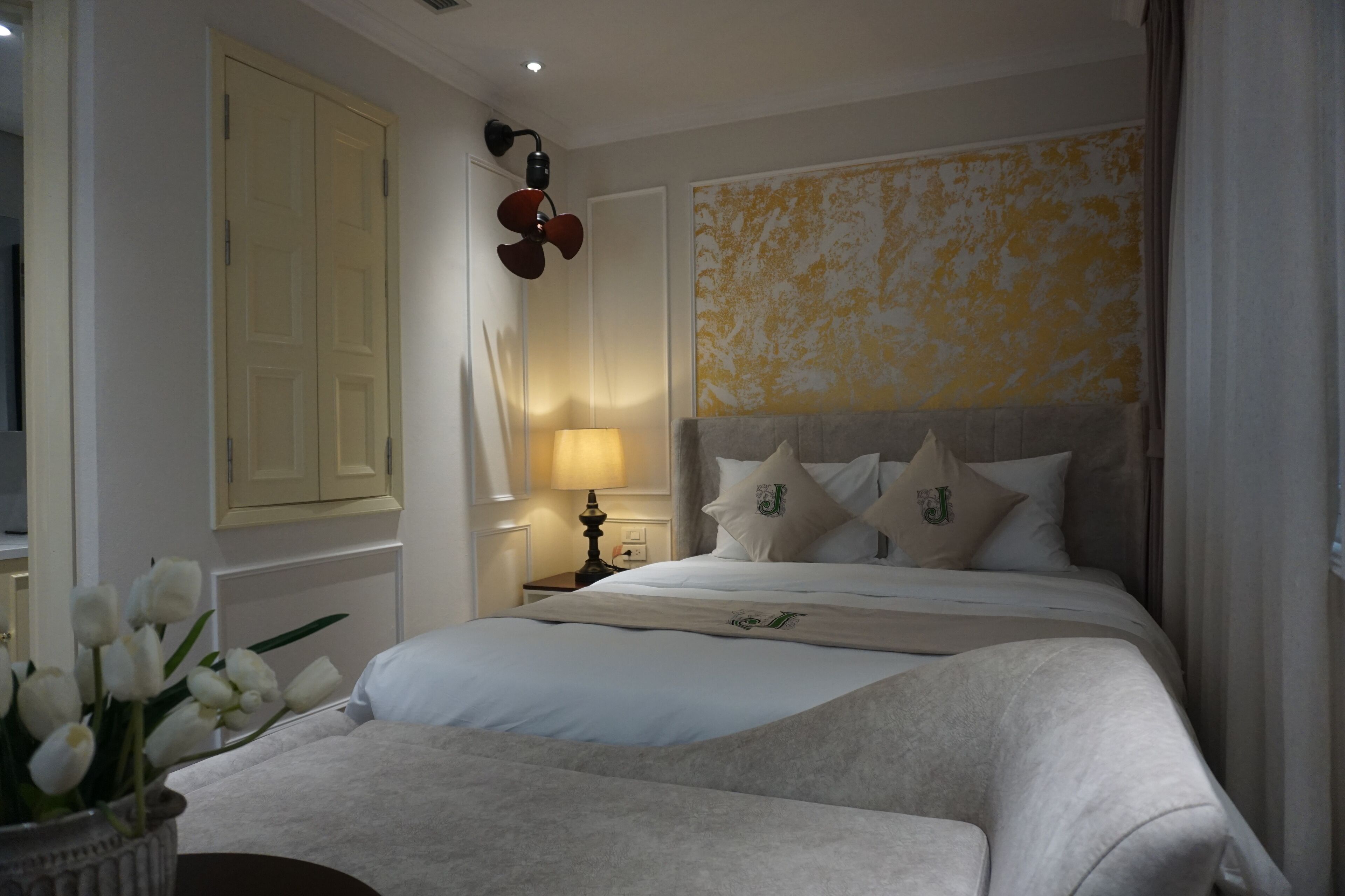 A hotel room with a large bed, a bedside table with a lamp, a vase with flowers, and a wall with a textured design.