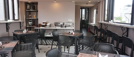 A restaurant with black and white tiled floors, black chairs, and tables set with cutlery and napkins.