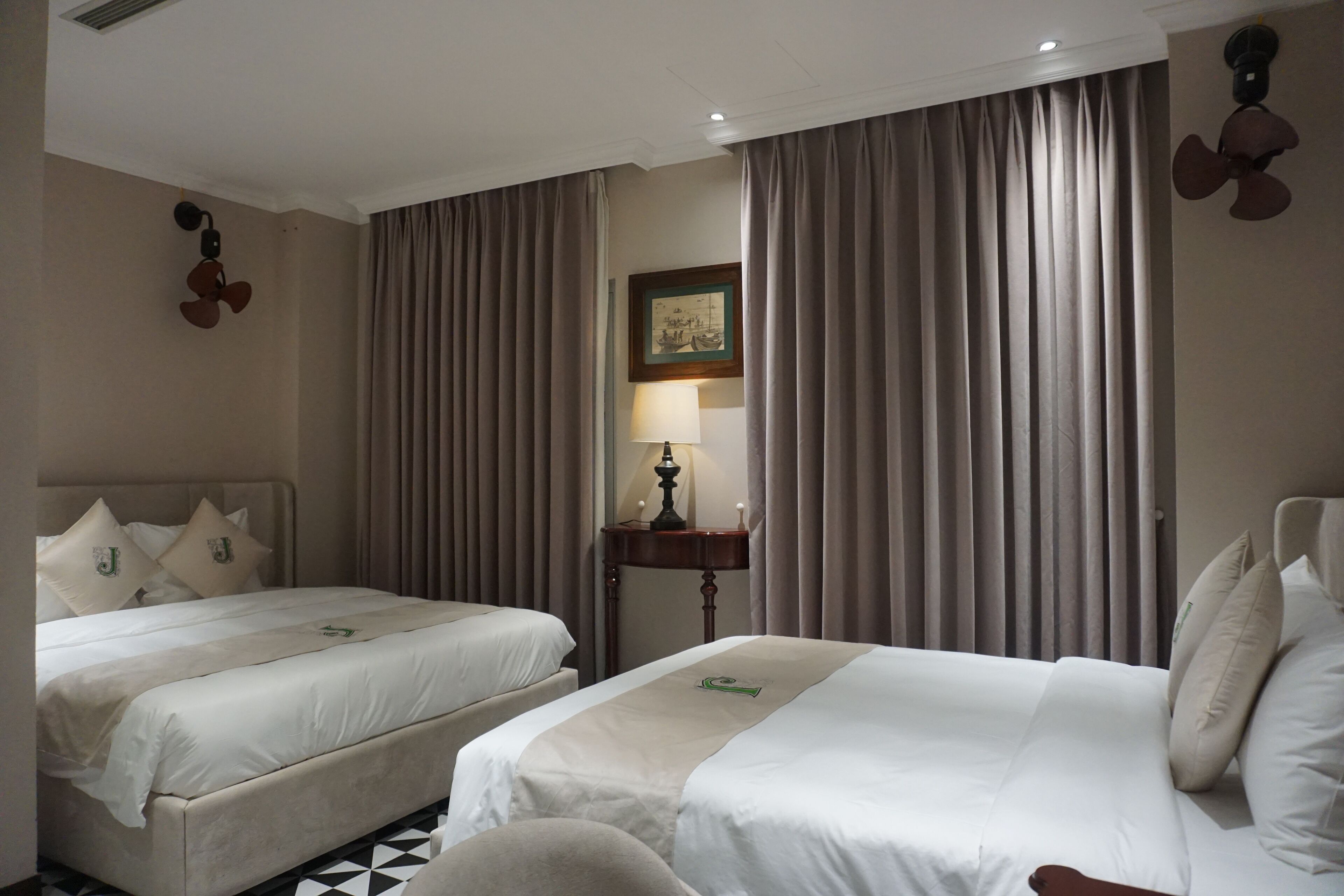 A hotel room with two beds, a nightstand with a lamp, and a window with curtains.