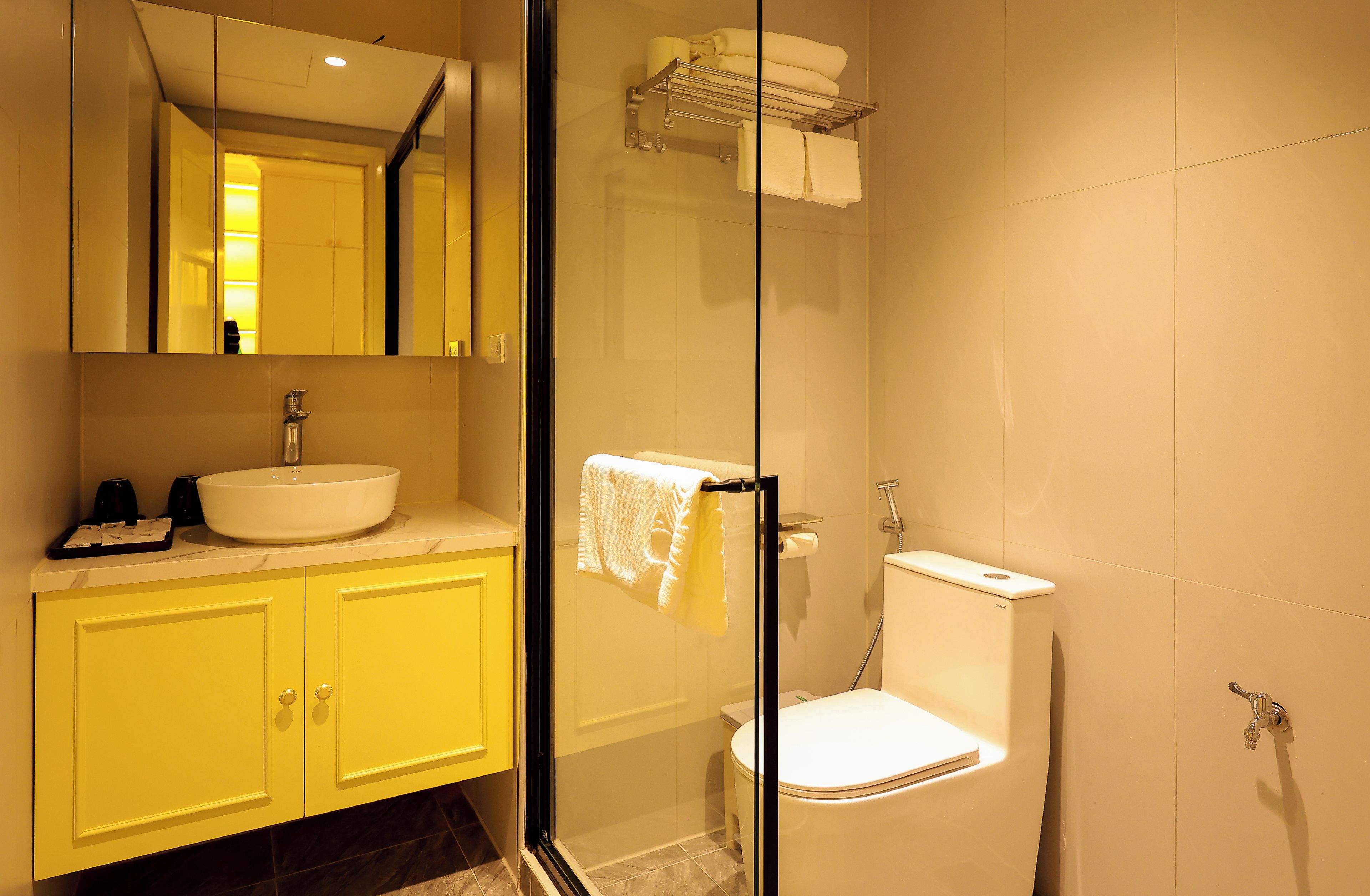 A bathroom with a glass-enclosed shower, a white sink, and yellow cabinets.