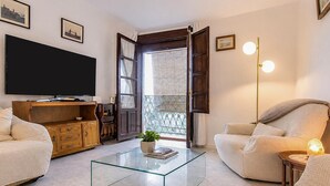A living room with a flat-screen TV, a glass coffee table, two beige armchairs, a wooden cabinet, and a balcony with a view. - Stunning apartment in Ronda with WiFi (Ronda)