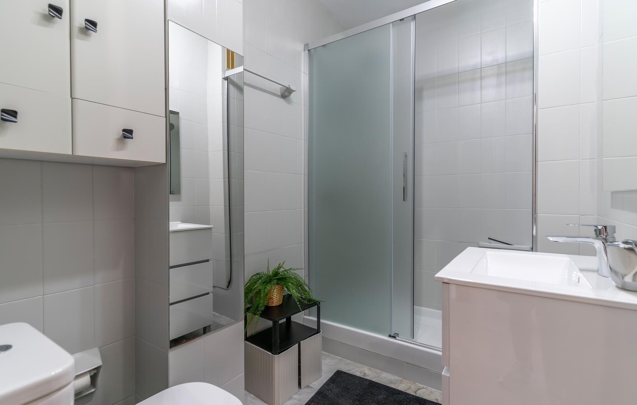 Et moderne badeværelse med en glasbrusekabine, en hvid vask og et toilet.