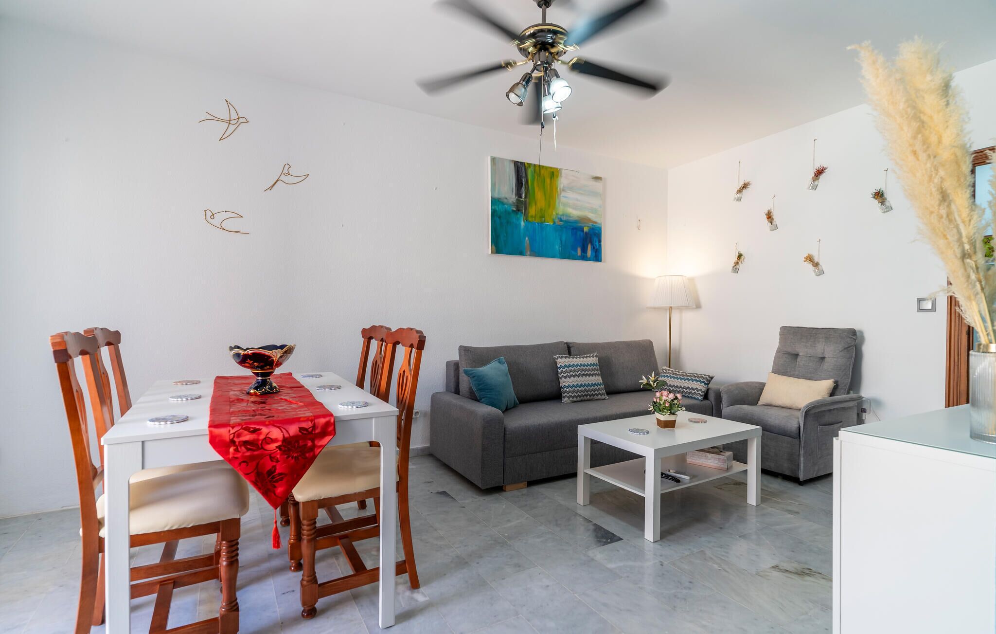 Ein modernes Wohnzimmer mit Essbereich, grauen Sofas, einem weißen Couchtisch und einem Deckenventilator.
