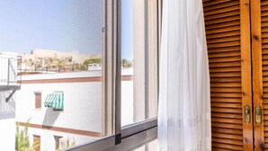 Ett fönster med ett metallnät, en vit gardin och träpersienner.