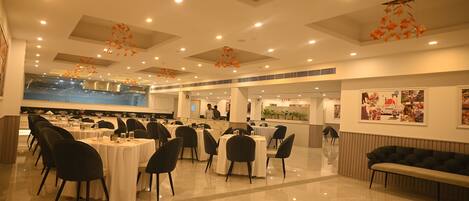 A spacious indoor dining area with multiple round tables and chairs, a central seating area with a bench, and ceiling decorations.