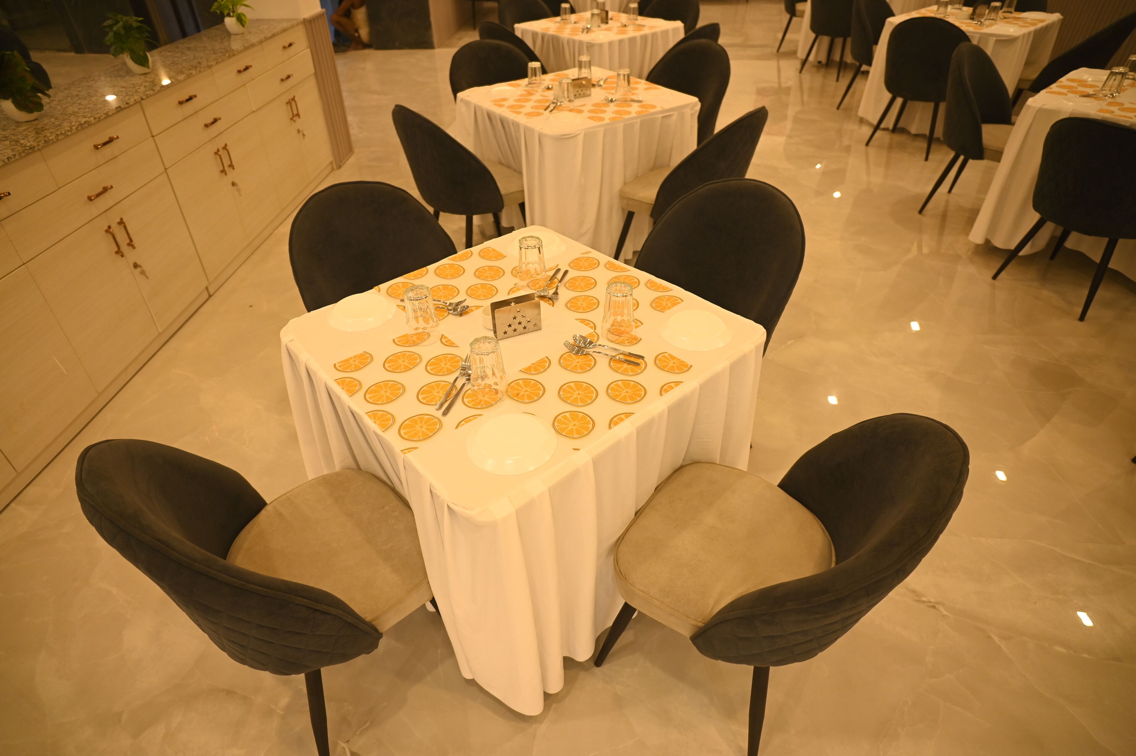 Een eetgedeelte met ronde tafels, zwarte stoelen en een witte tafelkleed met oranje dessins.