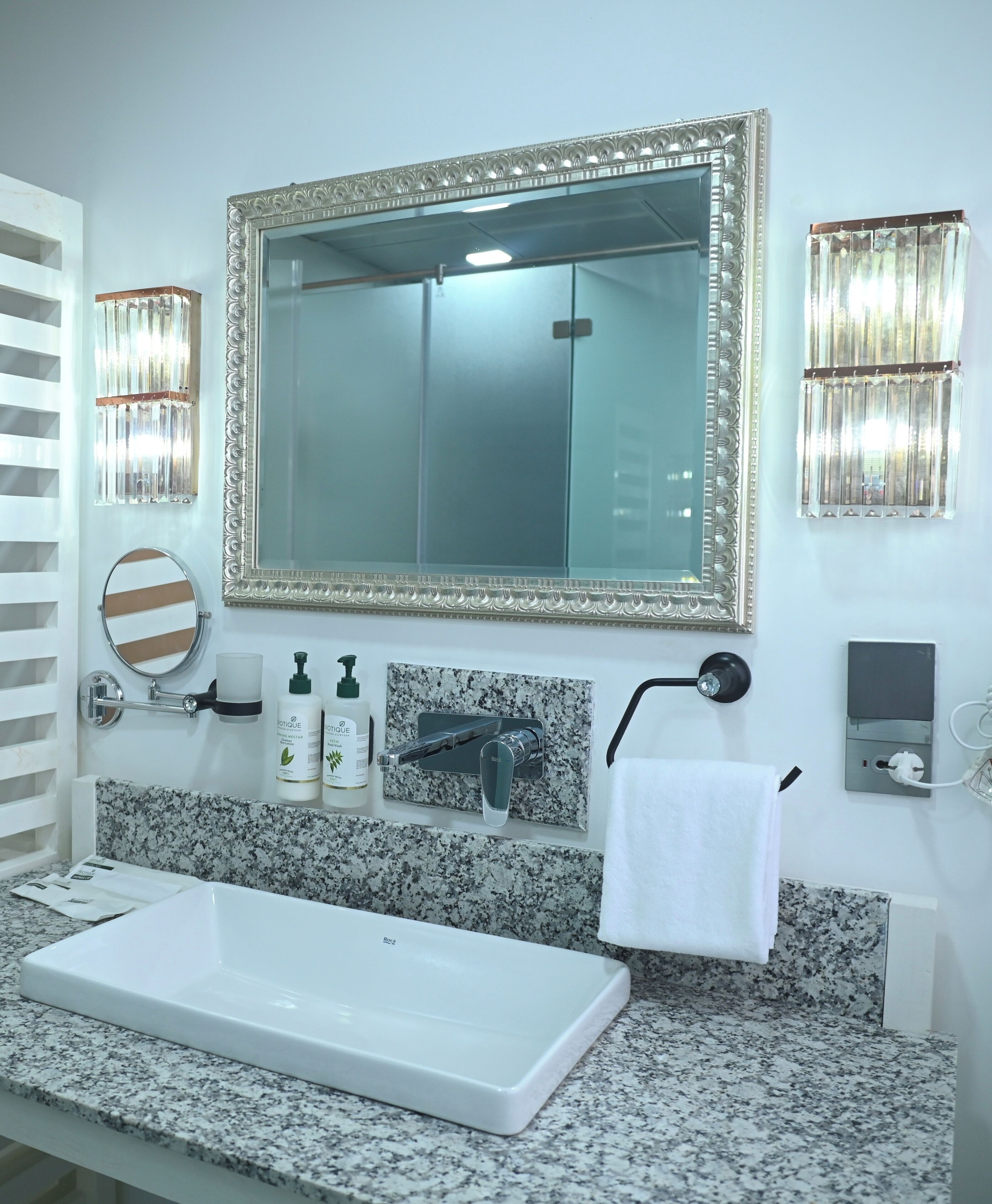 Une salle de bain avec un grand miroir, un lavabo, un porte-serviettes et deux lampes fixées au mur.