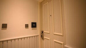 A hallway with a white door, a radiator, and two black plaques with numbers.