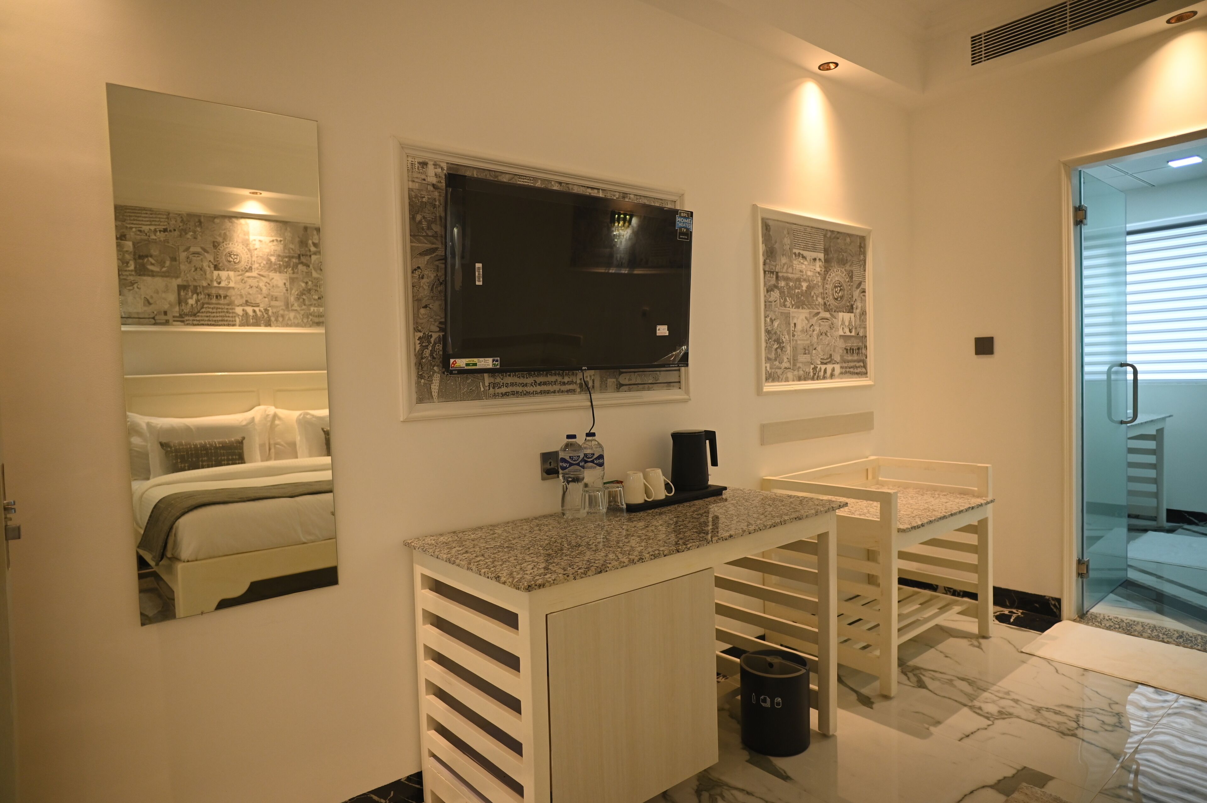 A modern bathroom with a large mirror, a flat-screen TV, and a small countertop with a coffee maker and toiletries.