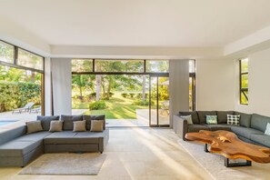 Un soggiorno moderno con un divano componibile, un tavolino in legno e ampie finestre con vista su un giardino.