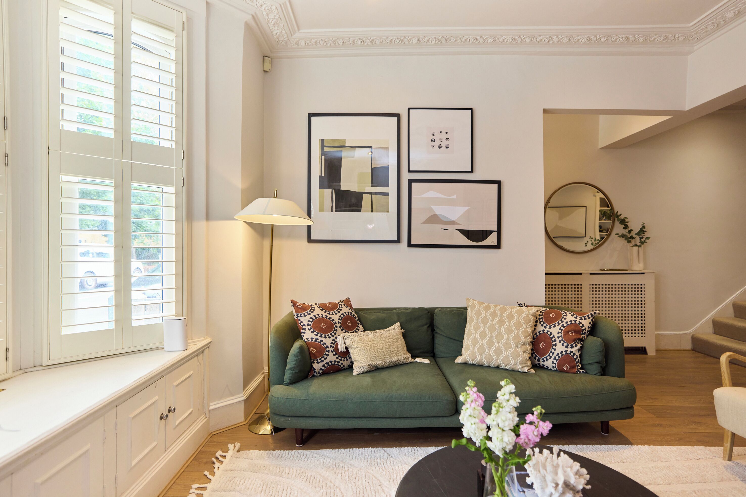 A green sofa with patterned cushions, a white lamp, and framed artwork on the wall.