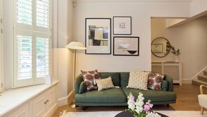 A green sofa with patterned cushions, a white lamp, and framed artwork on the wall. - The Battersea Park Townhouse (London)
