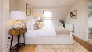 A bedroom with a large bed, a nightstand, a lamp, a window, and a radiator. - The Battersea Park Townhouse (London)