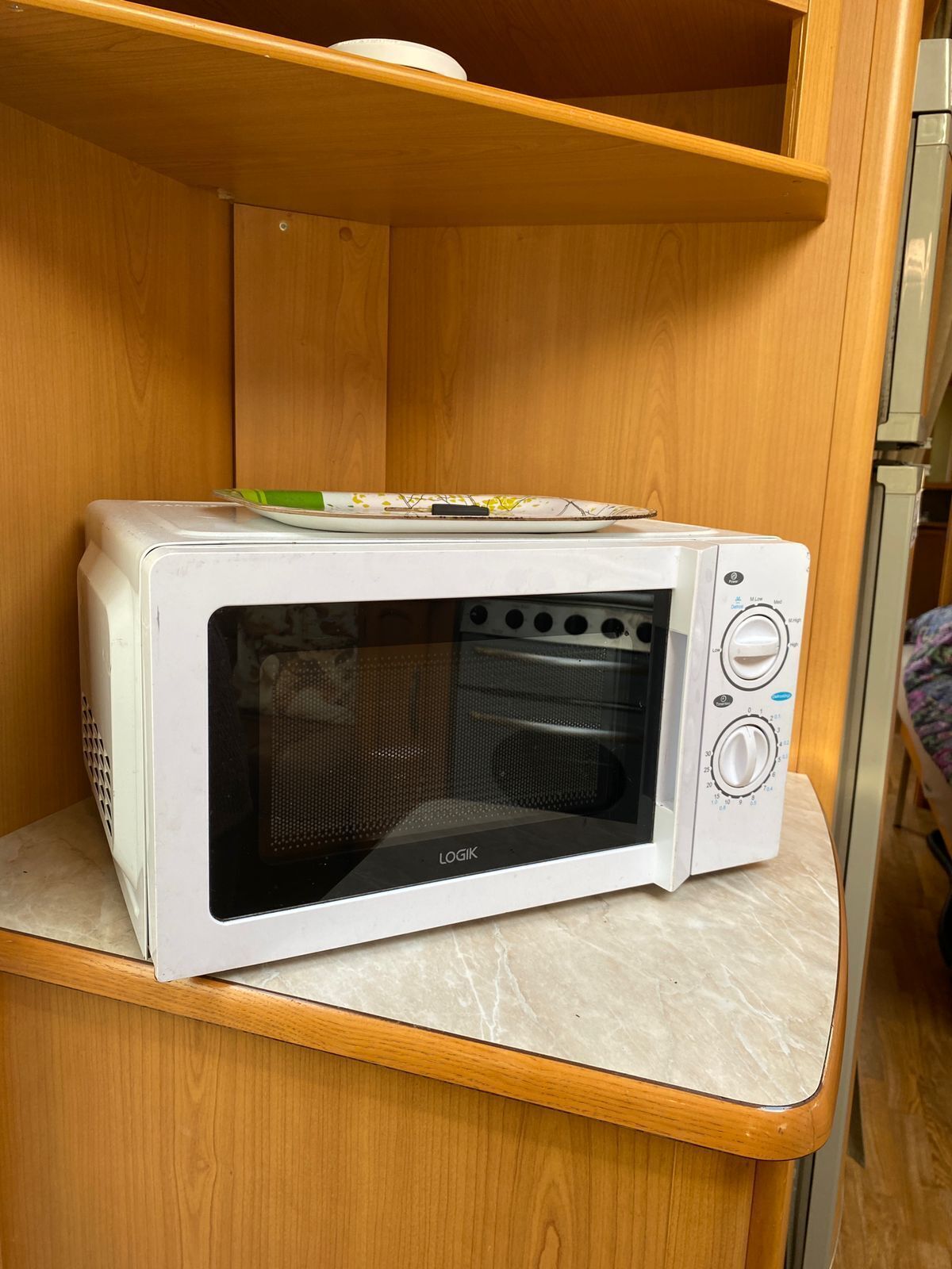 A microwave oven on a wooden shelf in a room.