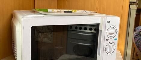 A microwave oven on a wooden shelf in a room.