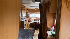A compact RV interior with a sleeping area, kitchenette, and a small dining space. - Cozy caravan in beautiful Tornio with AC (Lappi)